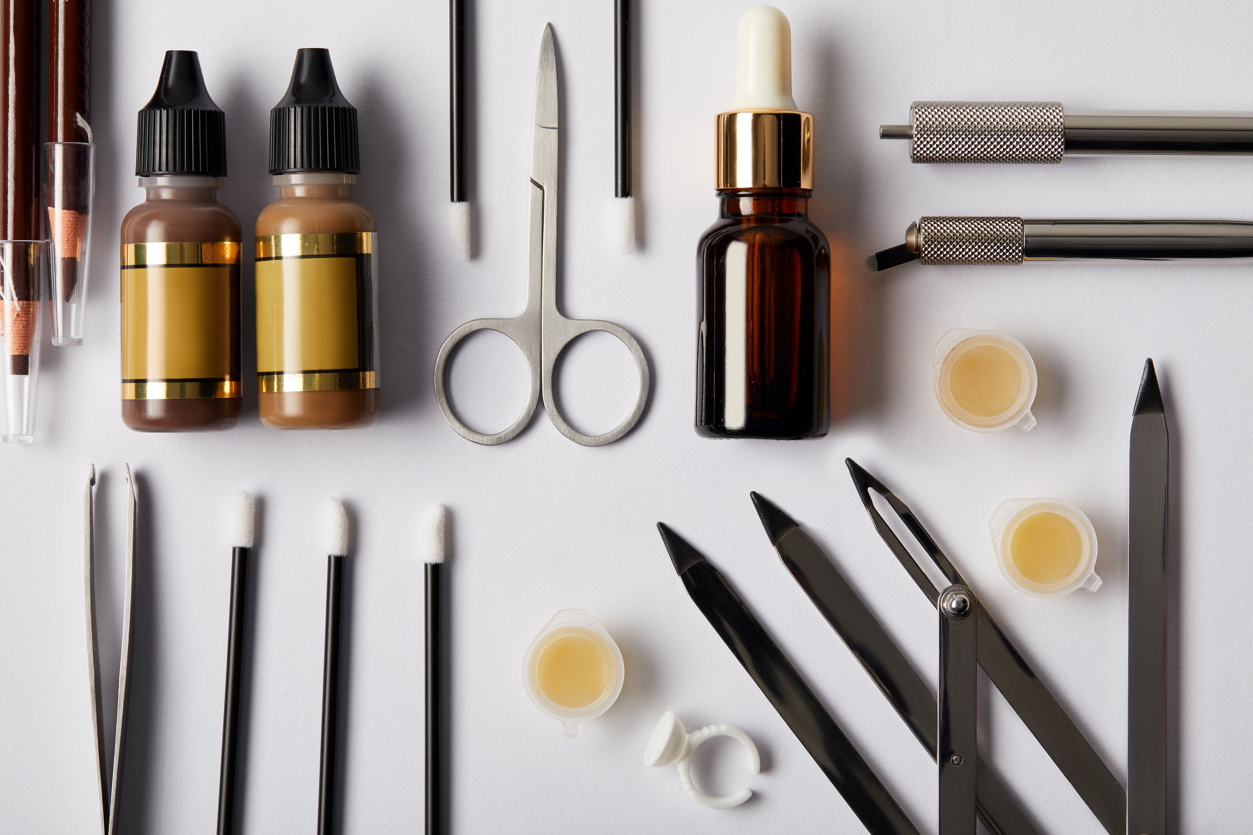 top view of various tools and cosmetics for permanent makeup on white